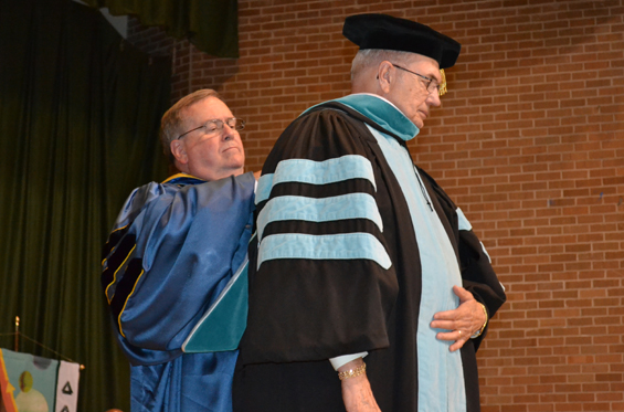 Delta State President Dr. John Hilpert (back) hoods Dr. Clyde Muse, bestowing  one of the university’s highest honors – an honorary Doctor of Science degree. 